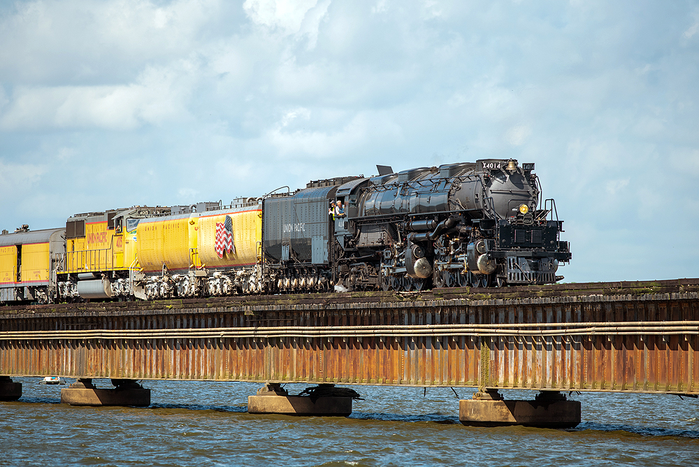 Large steam locomotive and train cross a causeway over water.