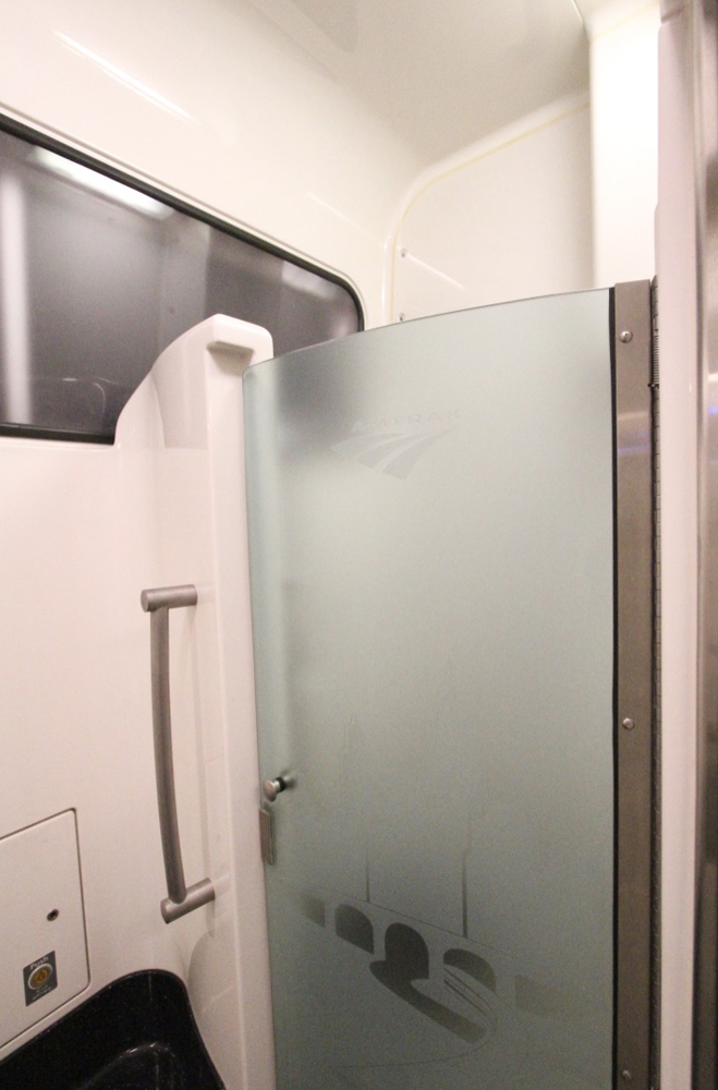 Shower on pasenger car with pink walls and smoked-glass door