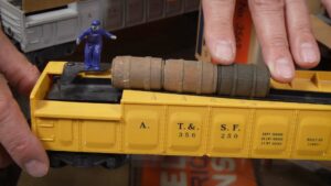 Close-up of yellow Lionel no. 3562 barrel car with barrels and worker.