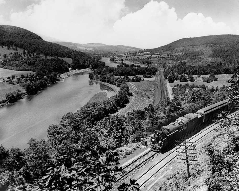 Steam locomotive with passenger train on hillside above river valley