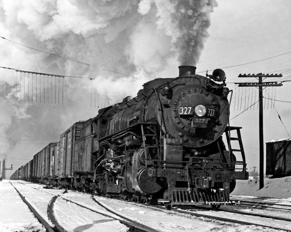 Steam locomotive moves freight train along snow-lined tracks