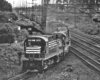 Black-and-white photo of road-switcher diesel locomotives leading freight train from multi-track main line to single-track branch line