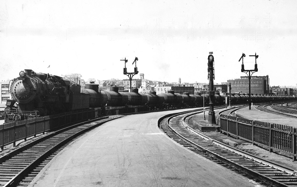 Black-and-white photo of steam locomotive with long train of tank cars