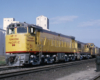 Three-quarter-angle color photo of two Union Pacific road-switcher diesel locomotives on freight train.