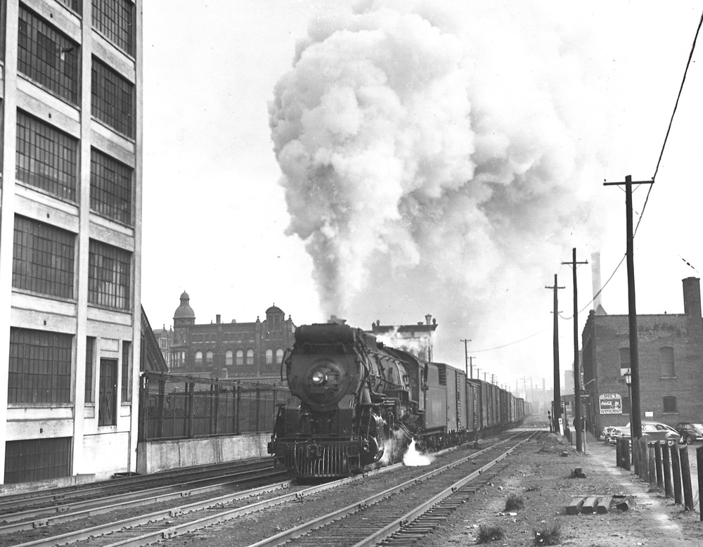 Black-and-white photo of steam locomotive with long train of boxcars