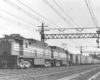 Black-and-white photo of two road-switcher electric locomotive with freight train