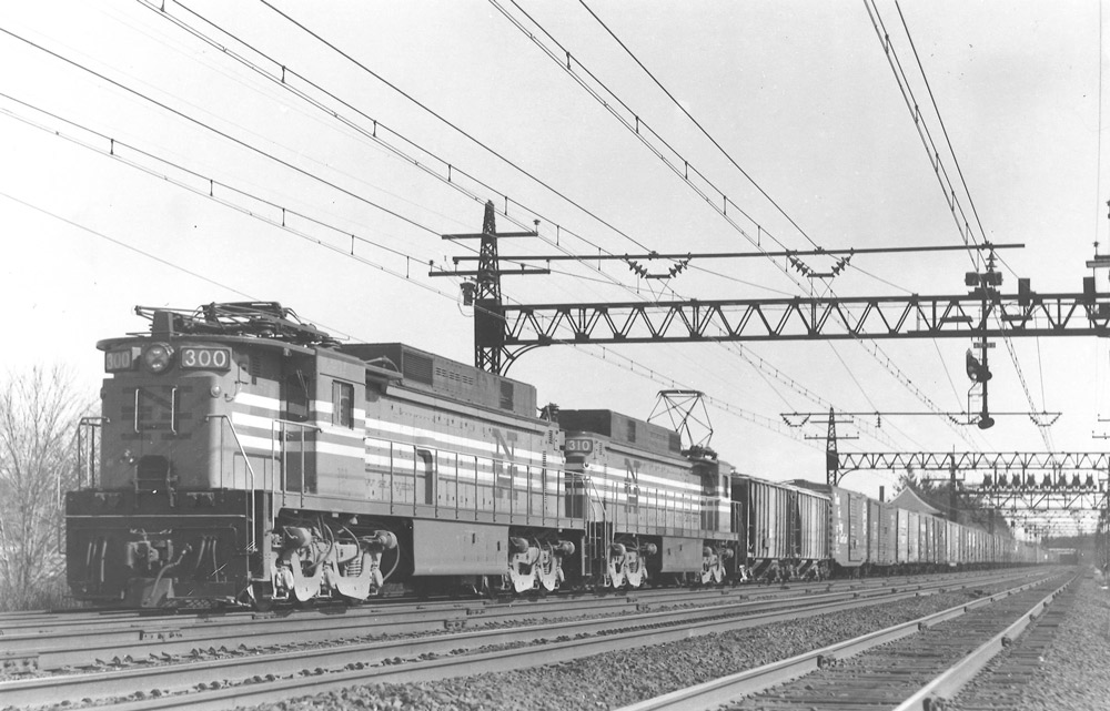 Black-and-white photo of two road-switcher electric locomotive with freight train