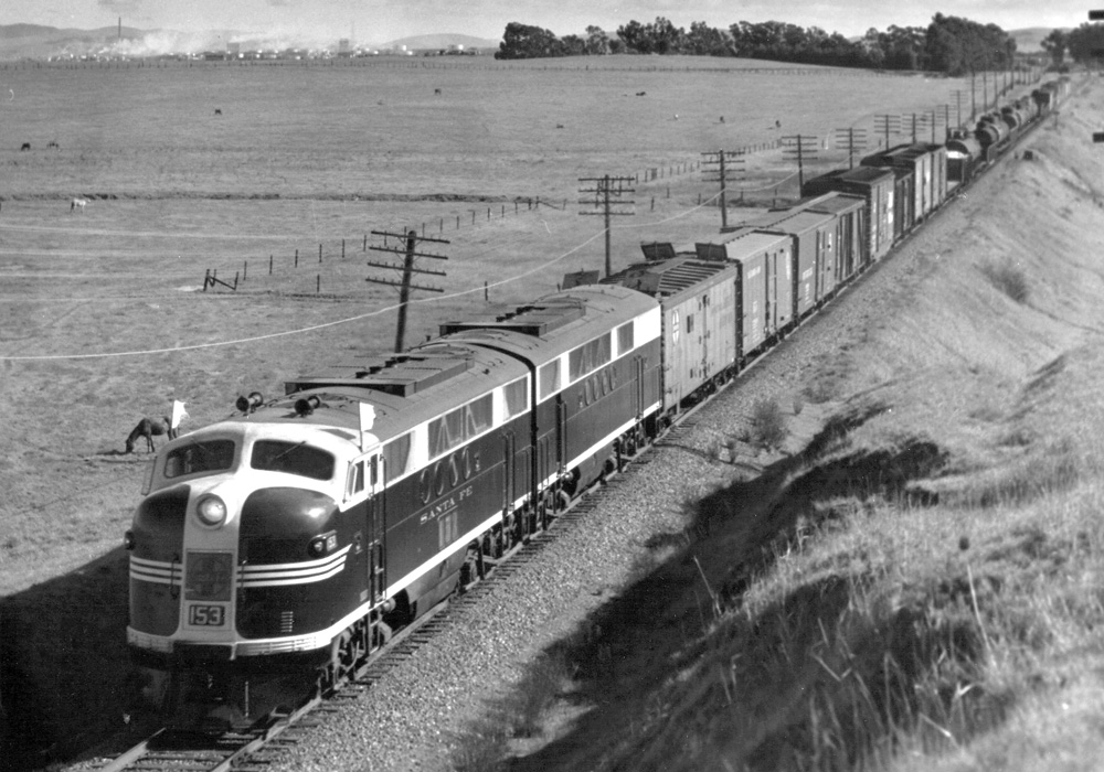 A black-and-white photo of a manifest freight train headed by a pair of EMD FT diesels running through the San Fernando Valley in California.