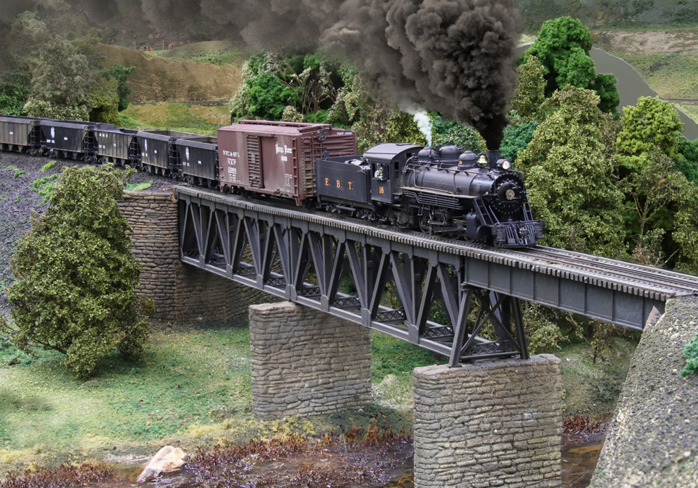 A narrow gauge steam locomotive pulls a train headed by an oversized-looking boxcar