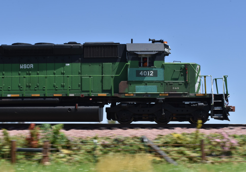 A green diesel locomotive bearing patched-out Wisconsin & Southern reporting marks rolls past motion-blurred scenery