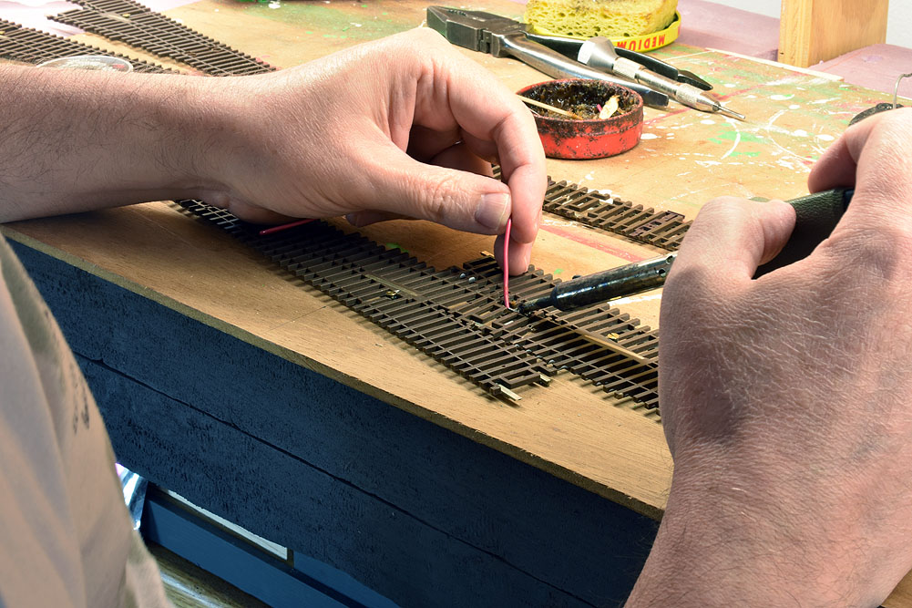 Red wire being soldered to bottom of rail joiner on overturned turnouts