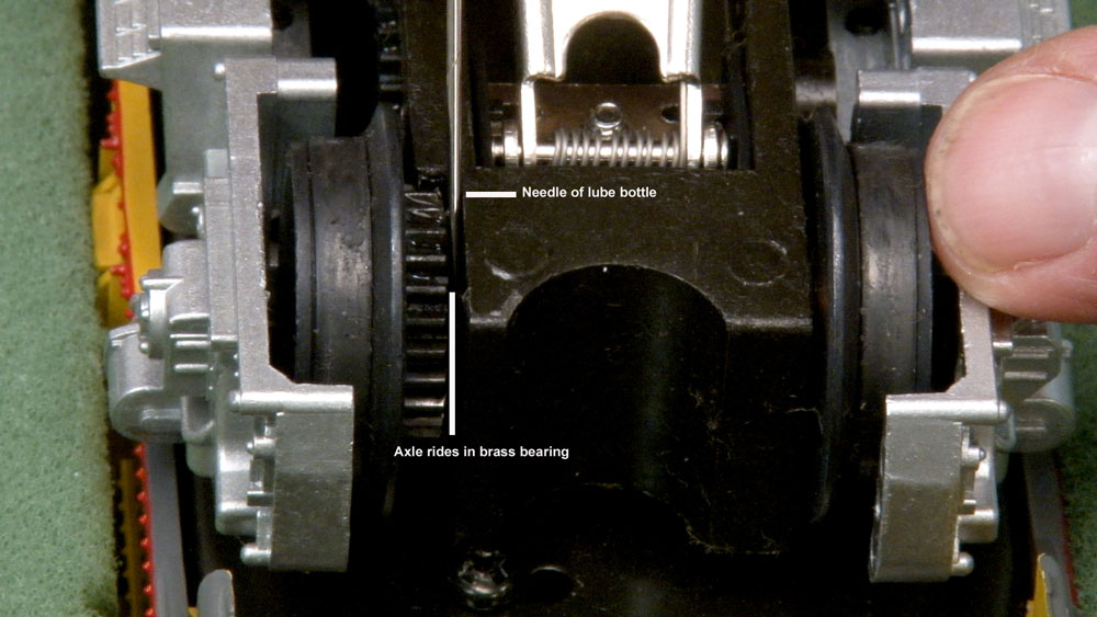 Pointing with a skewer at the gearing on the side of a model locomotive truck.