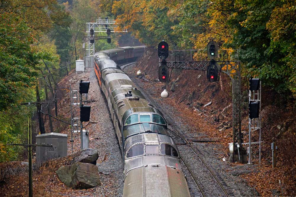 Passenger train dome cars pass signals among colorful trees