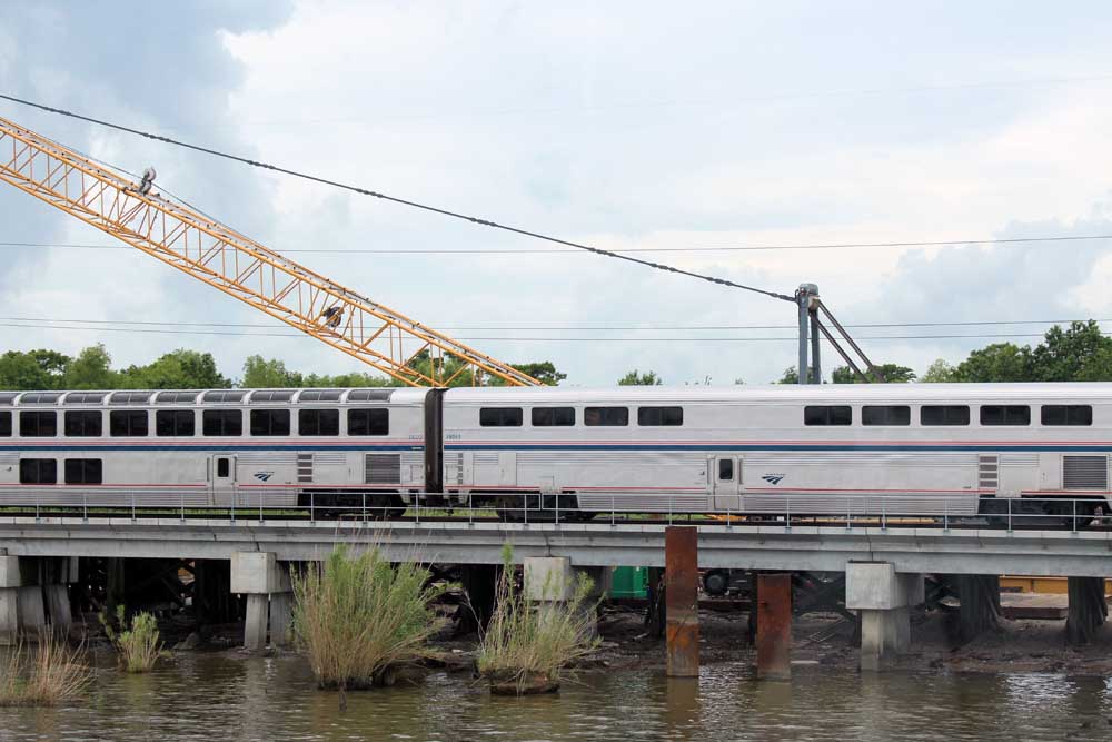 Bilevel passenger train on concrete trestle with construction crane behind it