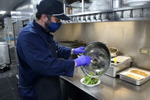 Man in mask cooks in railroad dining car kitchen