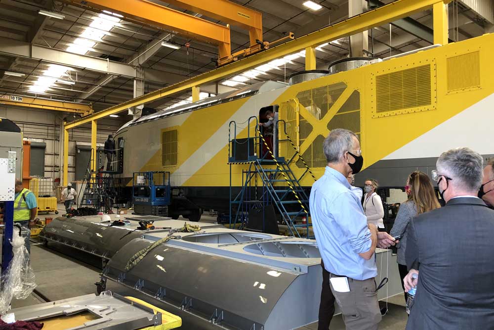 People in factory in front of yellow locomotive