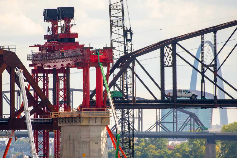 Red crane hovers over bridge truses in front of St. Louis Arch