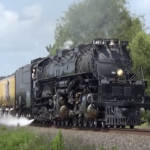 Large steam locomotive pulling a passenger train around a curve.