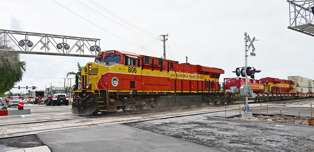 Red-and-yellow locomotives with fuel tender cross street