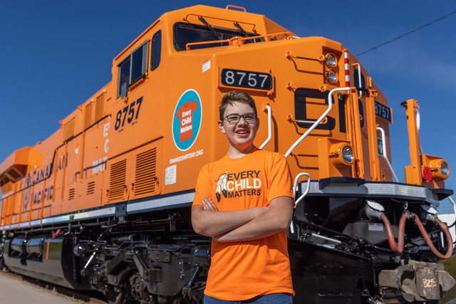 Boy in orange shirt standing in front of orange locomotive