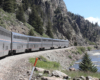 Train traveling along river with steep rock walls on either side