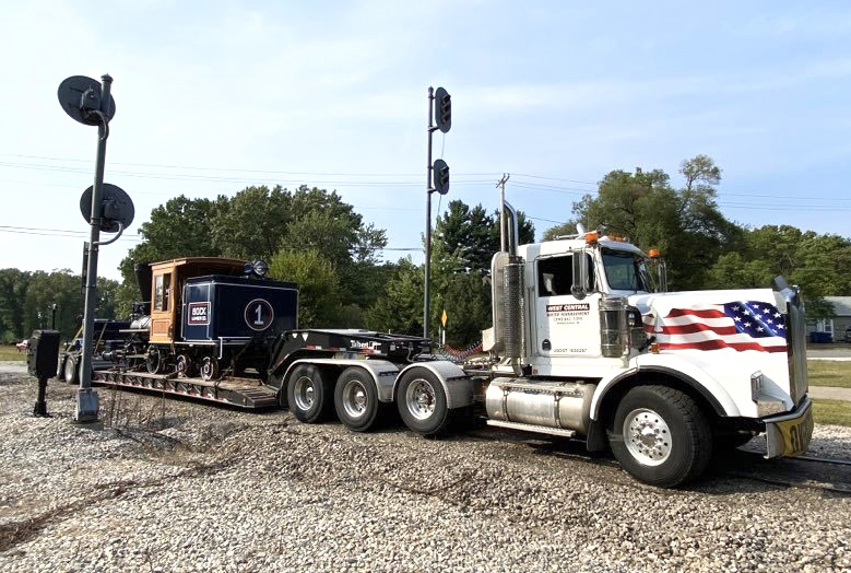 Small steam locomotive on truck with flatbed trailer