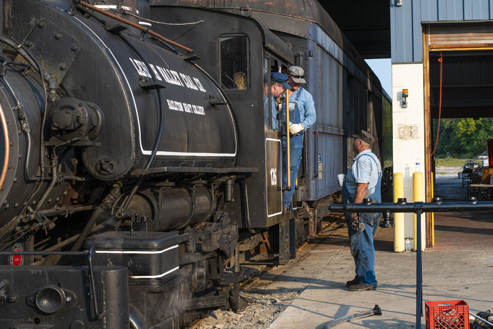 Crew members talk at cab of steam locomotive