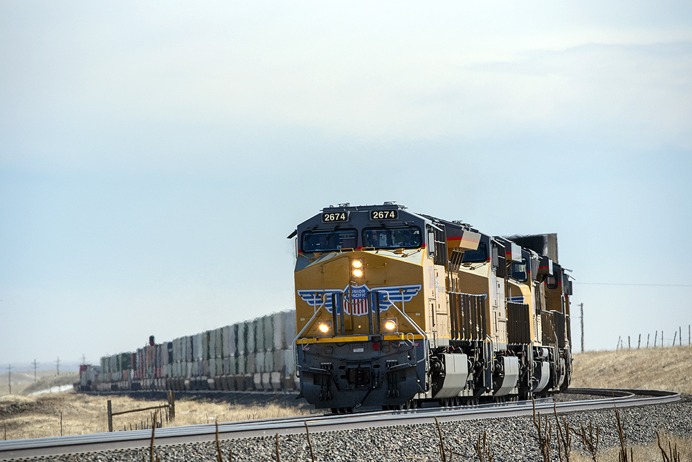 A yellow Union Pacific locomotive leads a freight trains over grasslands.