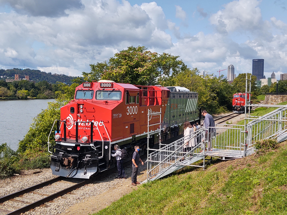 Red and gray locomotive parked on track along river