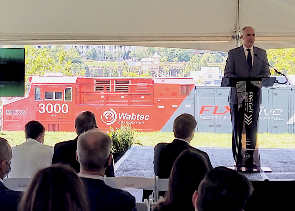 Man speaking at podium with locomotive in background