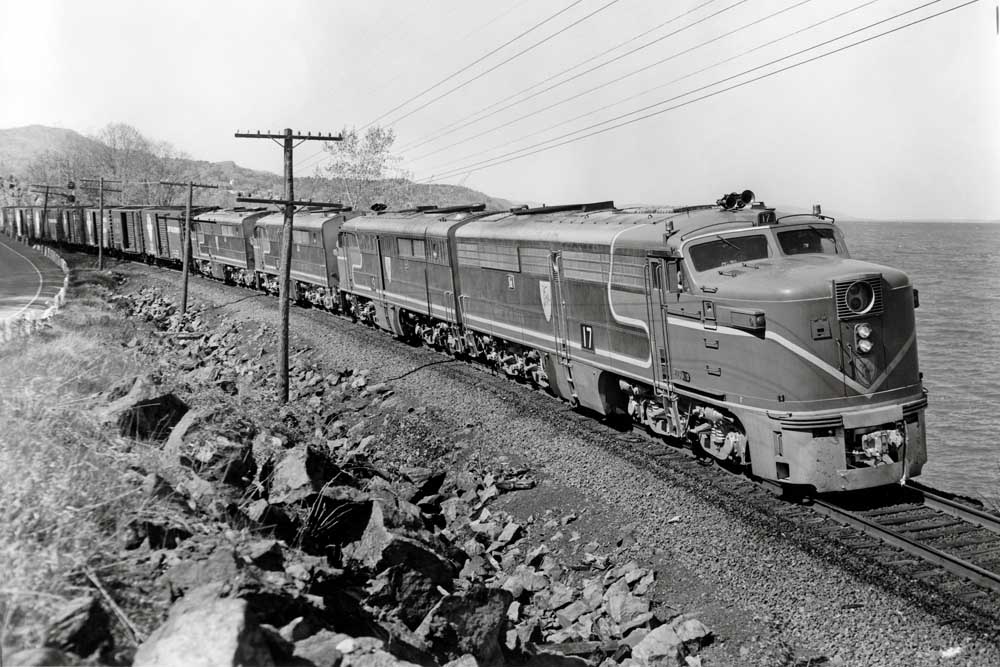 Streamlined passenger diesels haul freight cars along a waterfront