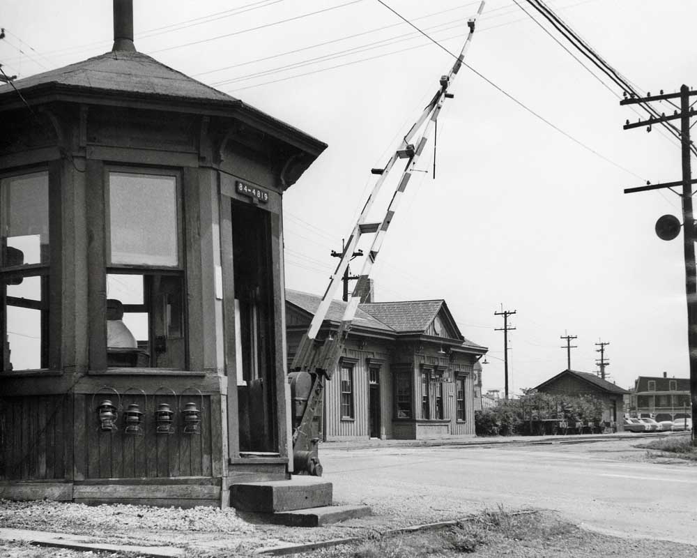 Octagonal watchman shanty and wooden crossing gates in front of wooden station