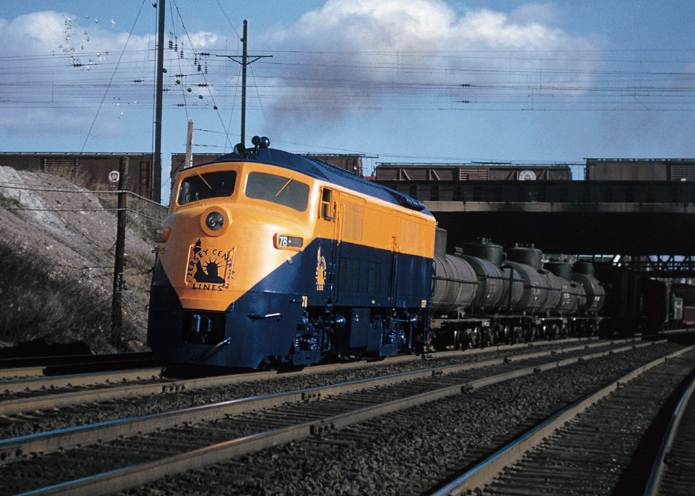 Orange and blue streamlined diesel locomotive with freight train under bridge