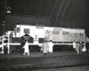 Black-and-white broadside photo of road-switcher diesel locomotive with hood doors open and people