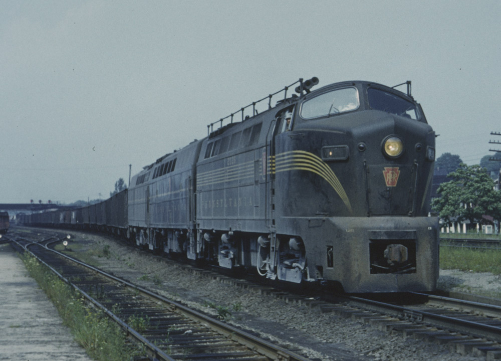 Green diesel locomotive with pointed nose and yellow stripes on freight train