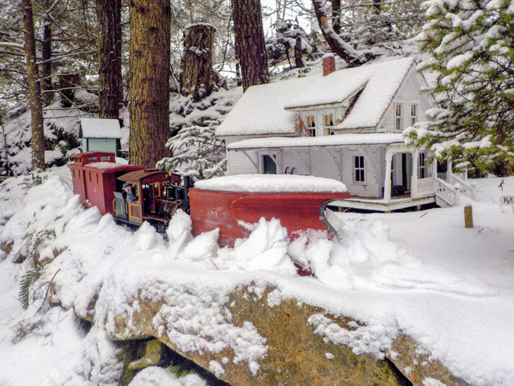 A model engine plowing snow on a garden railway