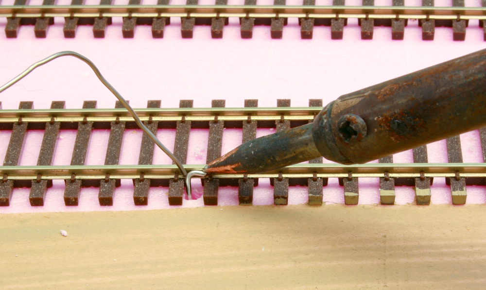 Soldering iron attaching wire to the side of track rail.