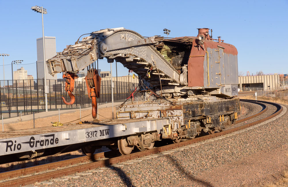 A brown-and-silver wreck crane is seen in transit, its boom secured to the deck