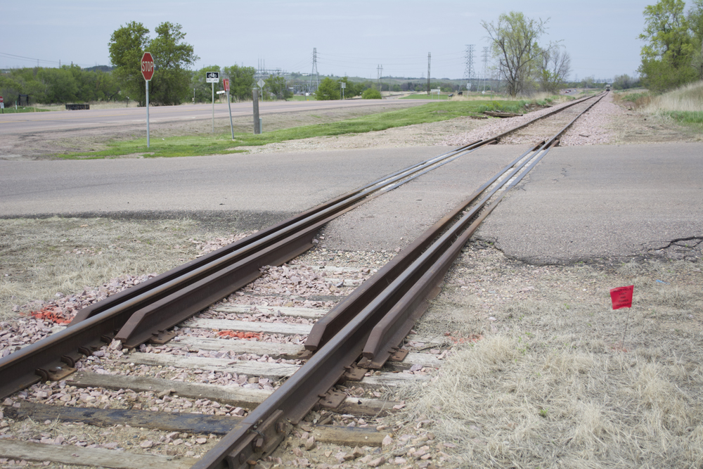 An asphalt-and-rail crossing near a t-intersection.