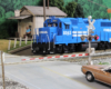 A bright blue Conrail diesel crosses a road in front of an old-fashioned white clapboard Post Office