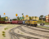 A modern yellow-and-gray diesel pulls a manifest freight past a busy highway lined with businesses