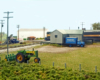 A pair of Monon diesels cross the Nickel Plate Road diamonds behind a freight house and a farm field where a green tractor sits