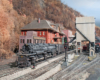 A steam locomotive pulls a string of flatcars loaded with military vehicles through an Appalachian town in autumn