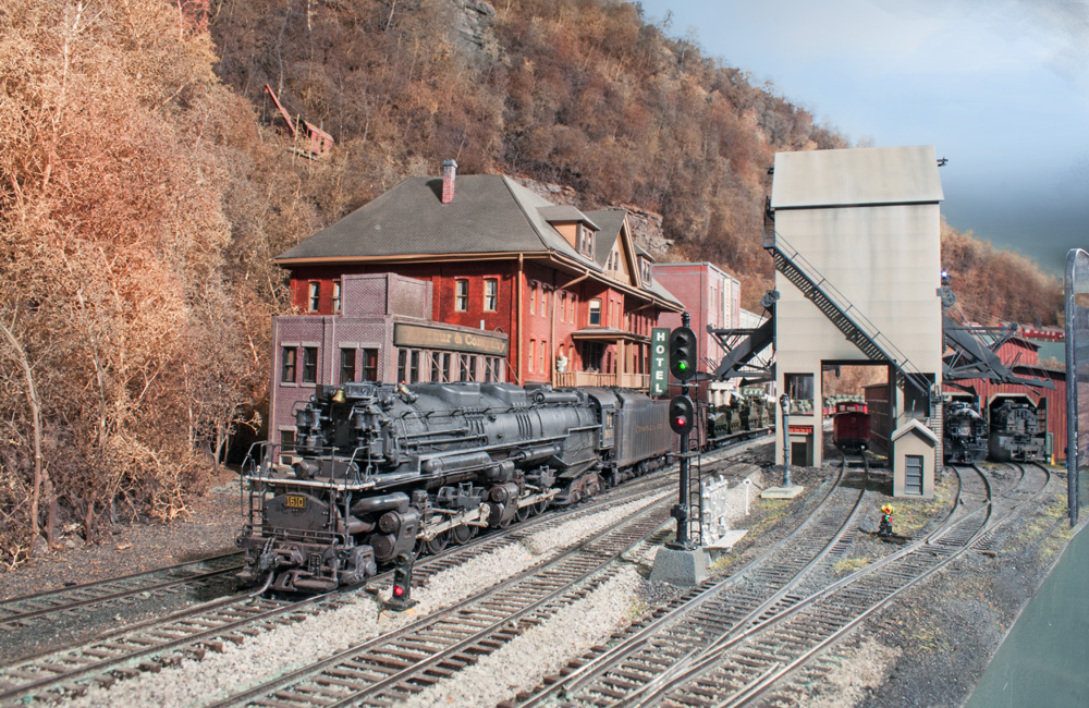 A steam locomotive pulls a string of flatcars loaded with military vehicles through an Appalachian town in autumn