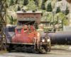 A weathered red-and-black diesel idles alongside an ash tower and a tank car in a yard