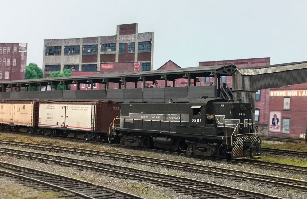 A black, silver, and white diesel pushes white refrigerator cars back alongside an icing platform