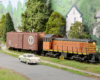An orange-and-black diesel switcher pulls a boxcar alongside a rural road
