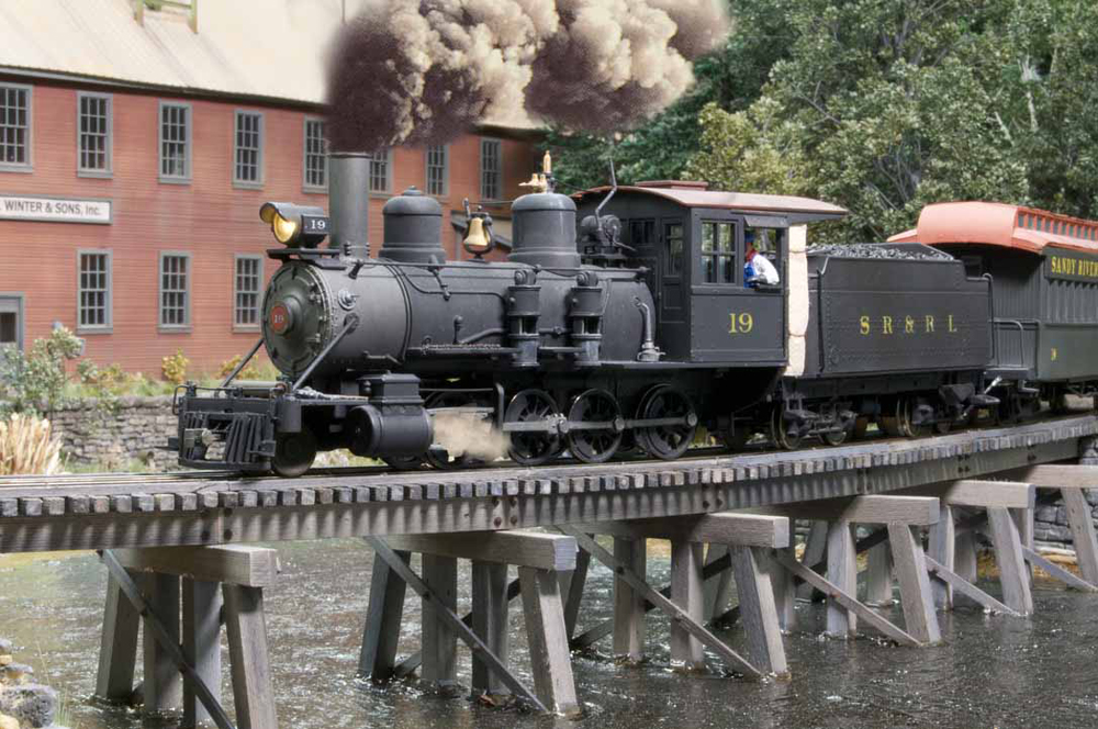 A smoking model steam locomotive crosses a bridge