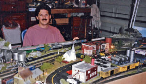 Man sitting next to an HO scale layout in a garage