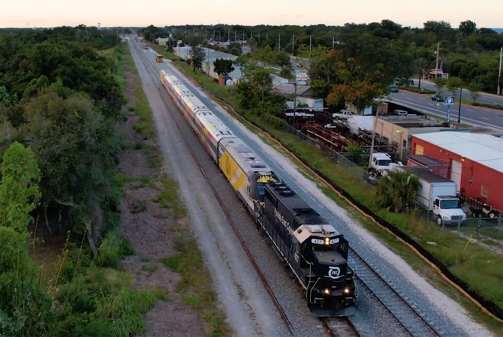 Aerial view of passenger train pulled by blue freight locomotive